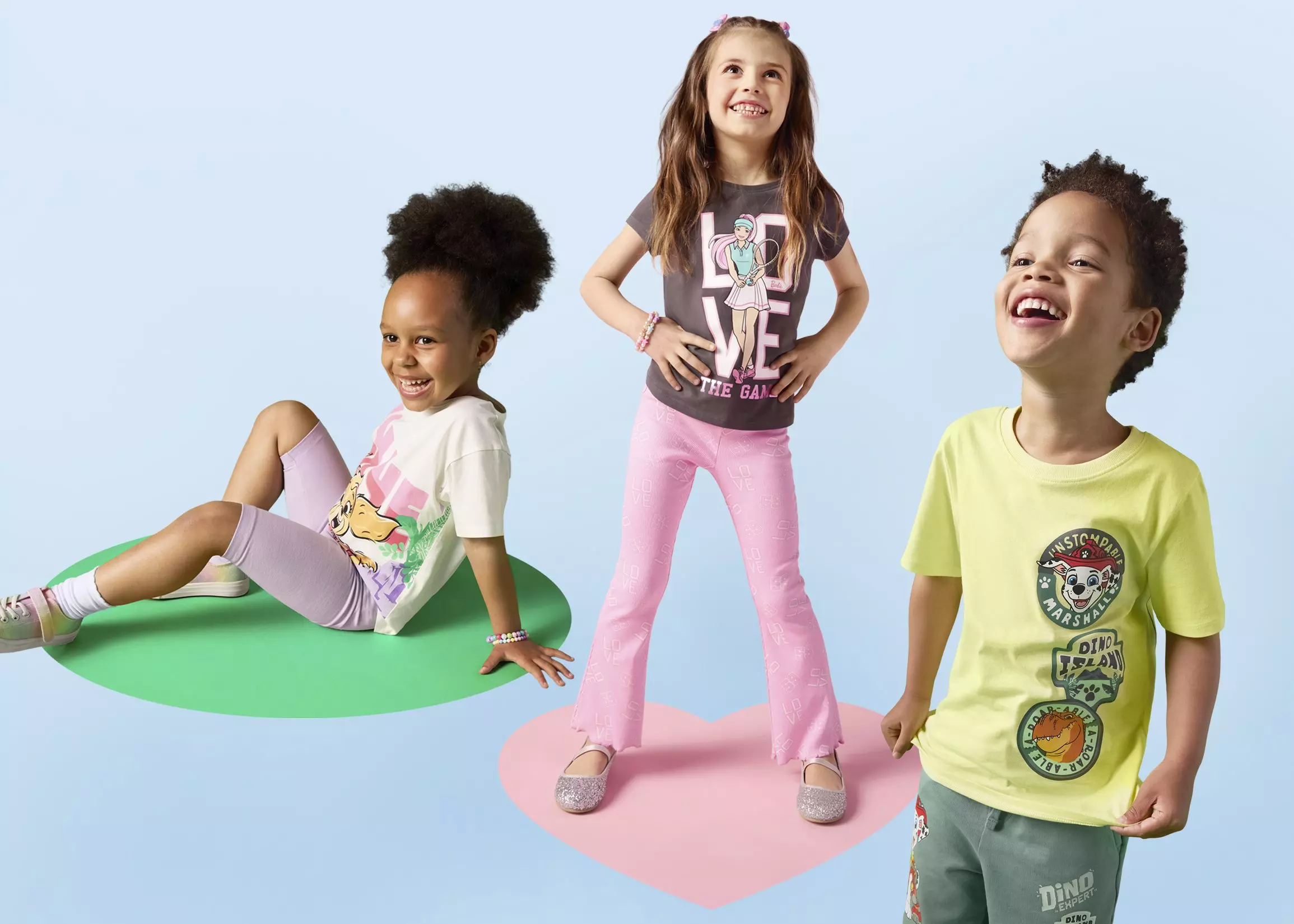 Tres niños sonrientes visten camisetas de personajes de Pepco con pantalones coloridos en poses alegres.